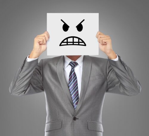 person wearing a grey suit holding a piece of paper on their face with a image of a stressed face drawn on it