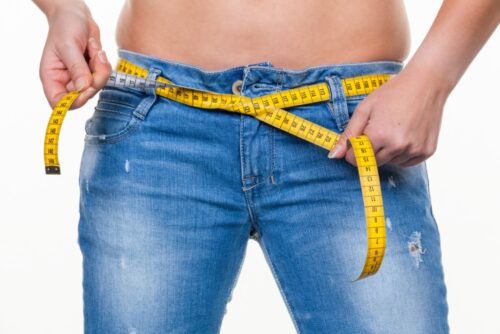 close up of woman's tummy and wearing faded blue jeans and tying a yellow tape measure around her waist