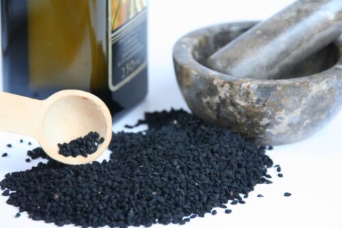 black seeds scattered with wooden spoon, mortar and pestle and bottle of black seed oil next to it