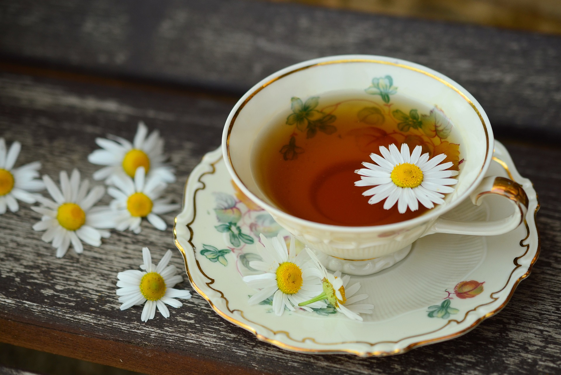 over the top view of a cup of chamomile tea on a saucer with fresh chamomile surrounding it on a wooden surface