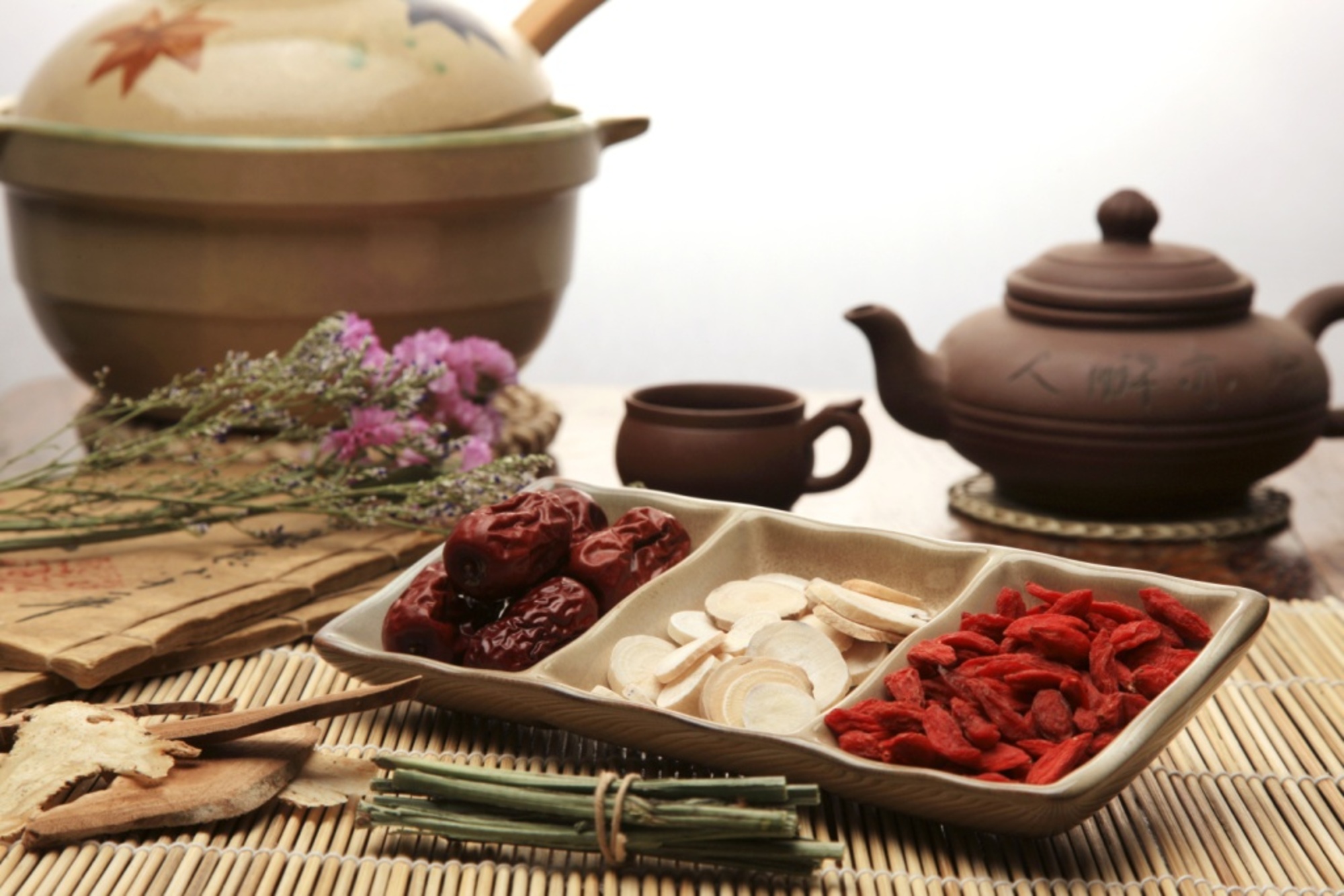 a selection of traditional Chinese herbs with a porcelaain brown teapot and cup and pot in the background