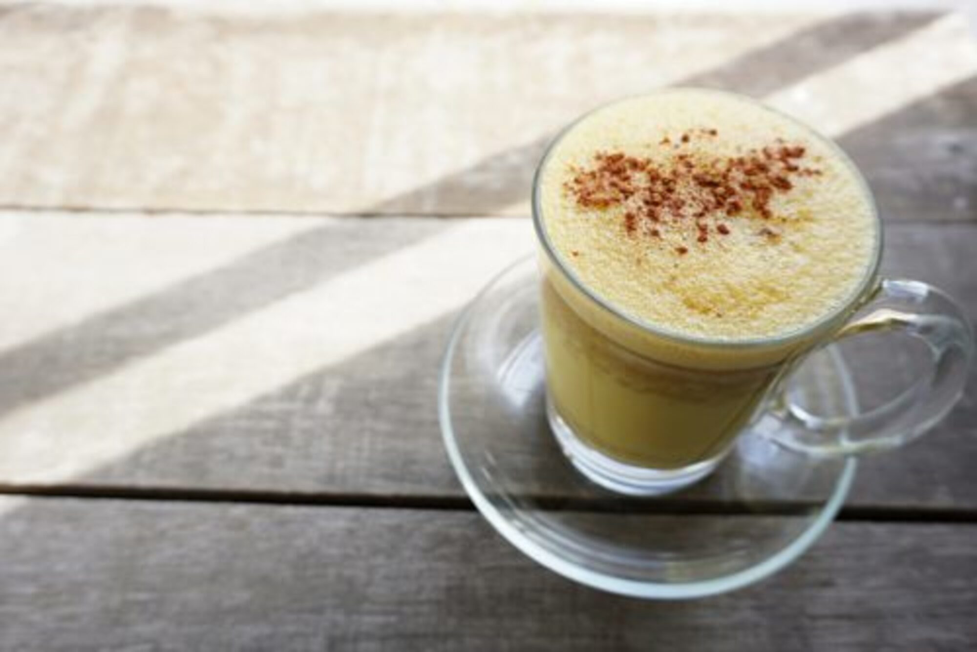 over the top view of a turmeric latte in a latte glass on a wooden table