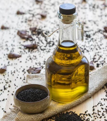 black seeds in a small metal bowl and a bottle of black seed il nearby. Black seed are scattered around them