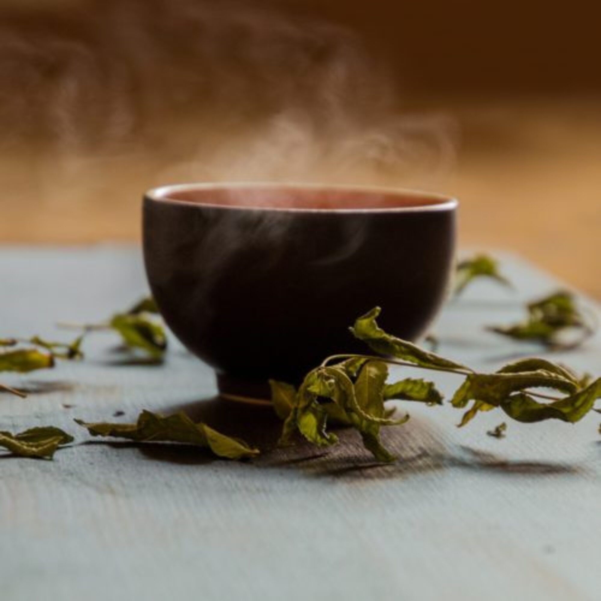 a dark steaming cup with dried green tea leaves scattered around it