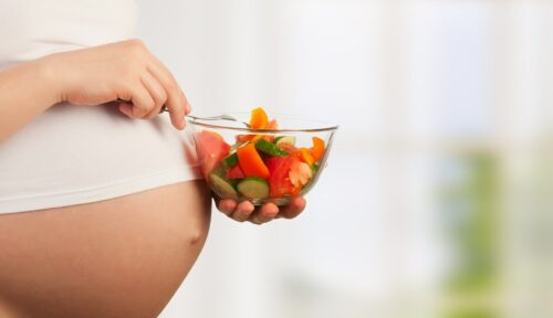 close up of woman's pregnant tummy and she is holding a bowl of fresh salad