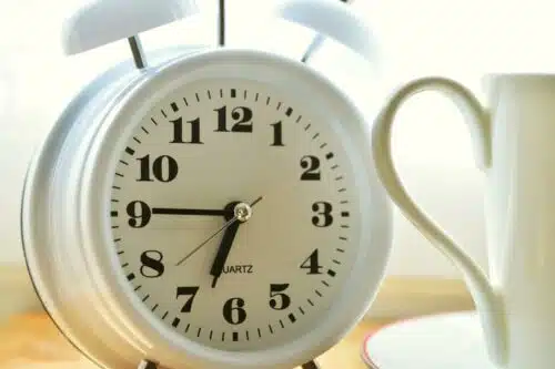 Close-up of a morning alarm clock next to a coffee mug, symbolizing habit shifts like choosing to drink more water first thing in the day.