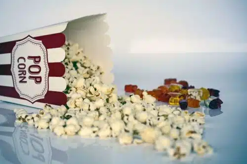 Close-up of movie popcorn spilling from a box with gummy bears in the background, showing how snacking habits fuel modern weight loss myths.