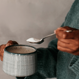 close up of woman holding ceramic cup and a spoonful of collagen powder