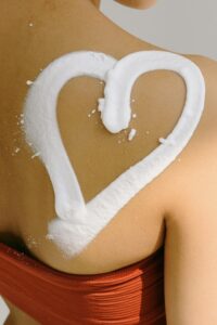 close up of womans' bare shoulder with cream in the shape of a heart on it