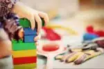 close up of child's hands playing with large lego pieces and various blurred objects in background