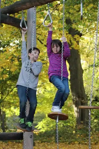 boy and girl climbing on a frame outdoors with trees in background