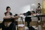 Stressed office workers surrounded by paperwork, with one woman asleep at her desk—visualizing emotional burnout symptoms at work.