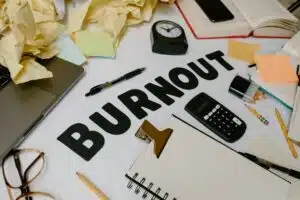 Desk cluttered with notes, coffee, and a burnout sign—symbolizing the overwhelm and emotional burnout symptoms faced daily.