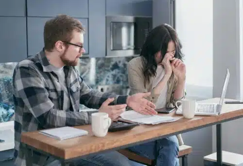 Couple in tense discussion over finances with documents and laptop, reflecting stress, conflict, and the question—Is your partner echoing your parent?