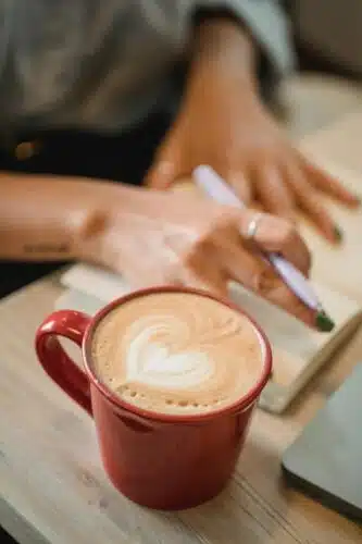Latte with heart-shaped foam beside hand journaling, symbolizing mindful reflection and inner work—Is your partner echoing your parent?